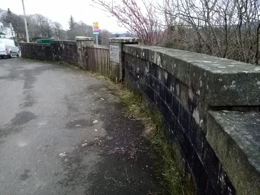 small car park next to a curving wall with metal gate