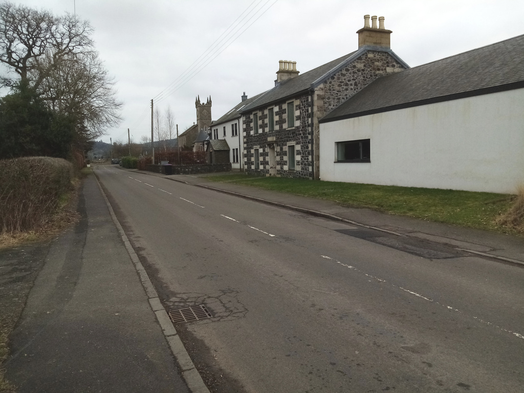 view of main road and rough stone building with church
     tower in background